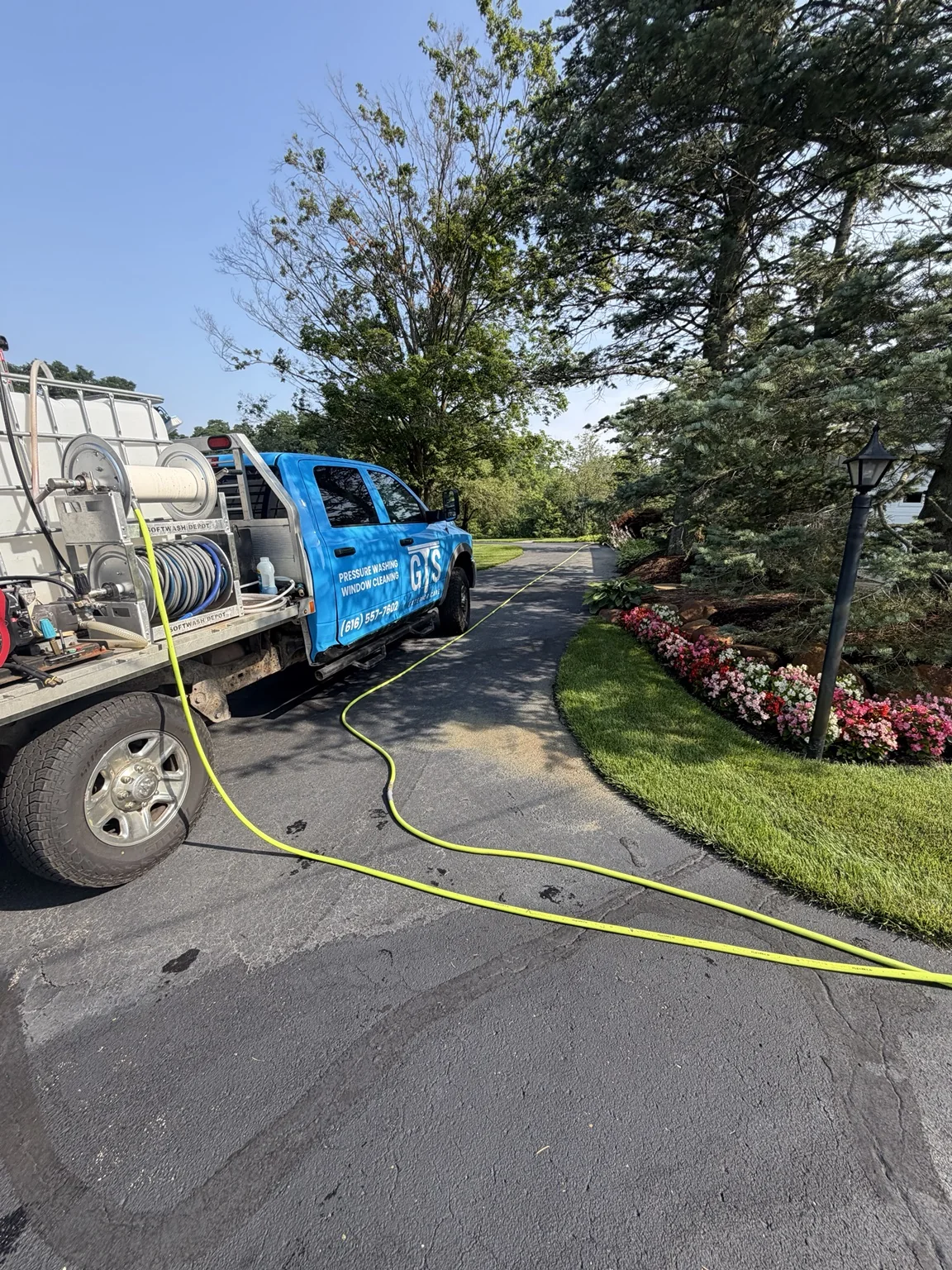 The blue GTS service truck with hose reels and a cleaning hose along a landscaped driveway